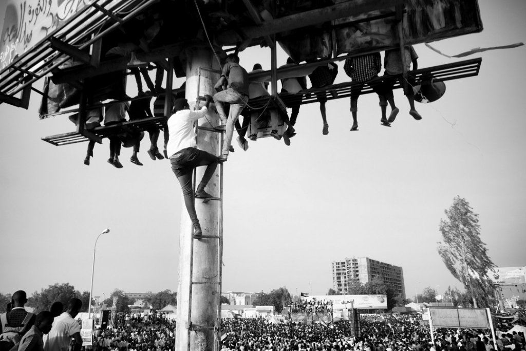 CAT 01 : Ahmed Ano. Des civils escaladent d’énormes panneaux publicitaires pour crier « Liberté, paix et justice ». Sit-in, quartier général militaire, Khartoum, 19 avril 2019. CAT 01 : Ahmed Ano. Des civils escaladent d’énormes panneaux publicitaires pour crier « Liberté, paix et justice ». Sit-in, quartier général militaire, Khartoum, 19 avril 2019.